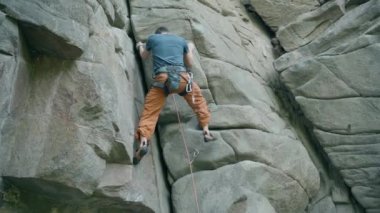 Güçlü kaya tırmanışçısı zorlu spor rotasına tırmanıyor, arıyor, uzanıyor ve sıkı tutunuyor. Dağcı sert bir hamle yapıyor ve halat kesiyor. Açık havada kaya tırmanışı ve aktif yaşam tarzı