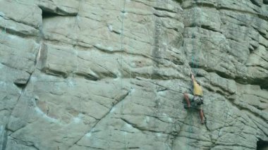 Güçlü kaya tırmanışçısı zorlu spor rotasına tırmanıyor, arıyor, uzanıyor ve sıkı tutunuyor. Dağcı sert bir hamle yapıyor ve halat kesiyor. Açık havada kaya tırmanışı ve aktif yaşam tarzı