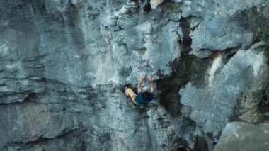 Atletik bir adam, sarkık bir kayaya halatla tırmanır, kurşun tırmanışı yapar. Dağ zemininde bir kaya tırmanıcısının silüeti. Açık hava sporları ve doğa eğlencesi. eğitim ve egzersiz