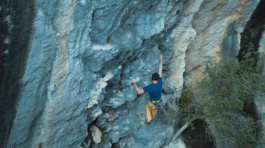 Tırmanışçı duvara tırmanır. Kaslı bir adam ağır çekimde kayaya tırmanır. Açık hava sporları. Kaya tırmanışı ve dağcılık, ekstrem sporlar.
