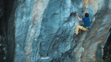 Tırmanışçı duvara tırmanır. Kaslı bir adam ağır çekimde kayaya tırmanır. Açık hava sporları. Kaya tırmanışı ve dağcılık, ekstrem sporlar.