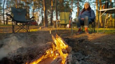Sıcak yürüyüş yapan kadın akşam vakti Güz Ormanı 'nda Şenlik Ateşi' nin yanında otururken dumanla yanıyor. Doğadaki şömine - geniş açılı çekim, yavaş çekim. piknik ve açık havada kamp.