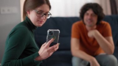Gözlüklü çekici bir kadın yakışıklı bir adamla odada selfie çekiyor. Kadın telefonla fotoğraf çekiyor.
