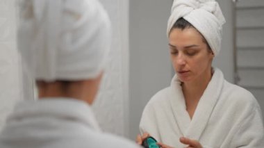 Göz kamaştırıcı bir bayan banyoda duruyor ve doğal cilt doyurucu bir maske takıyor. Cilt bakımı ayinlerinin güzelliği ve tazelenmiş hissetmek