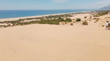 Akdeniz kıyısındaki Patara Sahili 'nde kumlu kumullarda yürüyen iki turist. Kum tepeleri, dağ sırtı ve mavi denizi olan çarpıcı bir çöl. Türkiye 'de güzel popüler bir yer