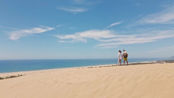 地中海沿岸の美しいパタラビーチで砂丘を歩くカップルの旅行者 山の尾根 青い海で素晴らしい砂漠 トルコで美しい人気スポット — ストック動画
