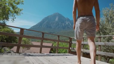 Vücut ağırlık kaldıran atletik yaşlı sporcu. Açık havada, tahta terasta vücut egzersizi yapıyor. Güzel dağ arkaplanlı spor egzersizi. aktif yaşam tarzı. mobil uygulama kullanılıyor