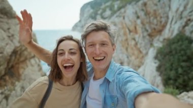 Mutlu çift, genç, gülümseyen kadın ve orta yaşlı adam deniz kenarında kayalık kanyonda yürüyüş yapıyor ve selfie çekiyorlar. Seyahat ve yaz tatili gezisi. Çekim için telefon kamerası kullanılıyor