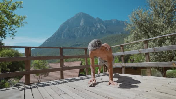フィットスポーツマンは 自然の中で屋外の木のテラスで運動をプッシュアップボディウェイトを行う 美しい山の背景を持つスポーツエクササイズ アクティブライフスタイル モバイルアプリのタイマータブ — ストック動画