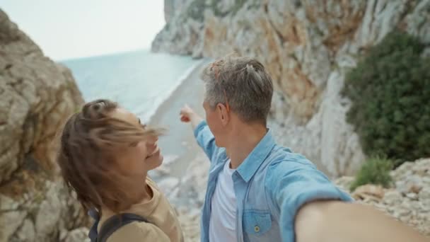 幸せな素敵なカップル若い笑顔の女性と海辺で岩の渓谷をハイキングし セルフィーを取る中年男性 ウォンダラスと旅行の夏休み旅行だ 撮影のために携帯電話カメラを使って — ストック動画