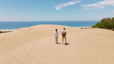 Akdeniz kıyısındaki Patara Sahili 'nde kumlu kumullarda yürüyen iki turist. Kum tepeleri, dağ sırtı ve mavi denizi olan çarpıcı bir çöl. Türkiye 'de güzel popüler bir yer