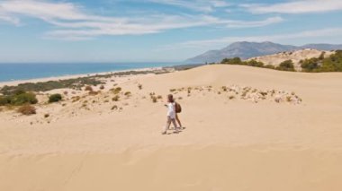 Akdeniz kıyısındaki Patara Sahili 'nde kumlu kumullarda yürüyen iki turist. Kum tepeleri, dağ sırtı ve mavi denizi olan çarpıcı bir çöl. Türkiye 'de güzel popüler bir yer