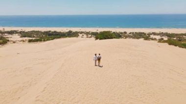 Akdeniz kıyısındaki Patara Sahili 'nde kumlu kumullarda yürüyen iki turist. Kum tepeleri, dağ sırtı ve mavi denizi olan çarpıcı bir çöl. Türkiye 'de güzel popüler bir yer