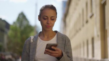Şehir manzarası. Sokakta cep telefonu kullanan bir iş kadını. Güzel bir iş kadını cep telefonuna bir mesaj yazıyor. Akıllı telefon kullanan gri ceketli melez kadının portresi.