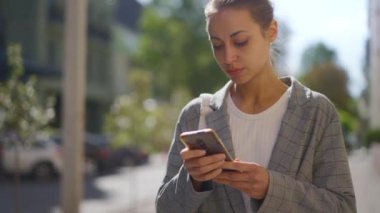Şehir manzarası. Sokakta cep telefonu kullanan bir iş kadını. Güzel bir iş kadını cep telefonuna bir mesaj yazıyor. Akıllı telefon kullanan gri ceketli melez kadının portresi.