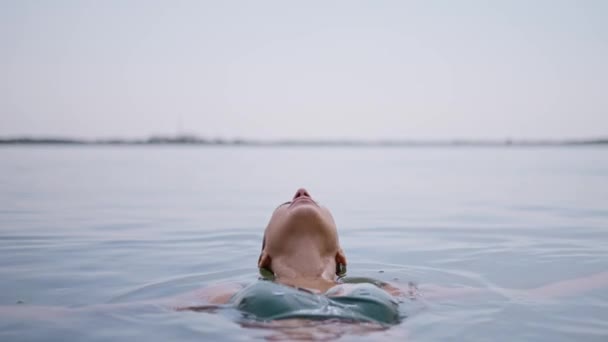 年轻的成年女子放松地躺在湖面上 心满意足地闭上眼睛 享受着泡在水里的乐趣 站在水面上的女人 年轻的模特儿沉入大海 热带假期的享受 — 图库视频影像
