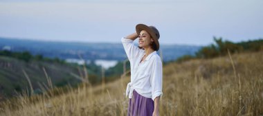 Panoramik sakin yamaçlarda zarif, şık şapkalı genç bir kadın akşamları doğada kaliteli zaman geçiriyor.