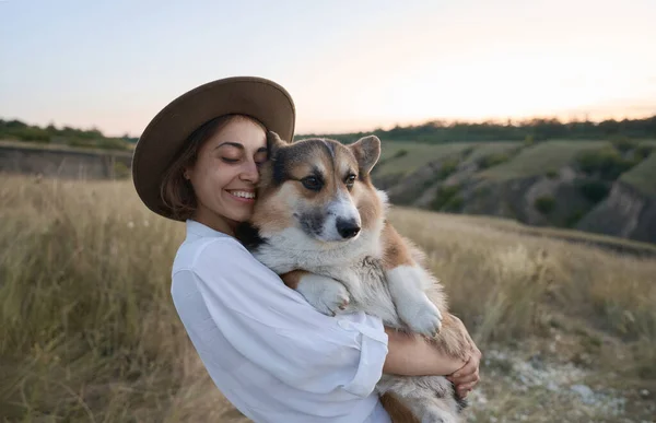 Elegant young woman tenderly embracing her pet Corgi dog outdoors. Cute moments and friendship between human and animal