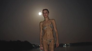 Yılan desenli bikinili güzel, genç ve seksi bir kadın her gece denizde yüzüyor. Modaya uygun bir modelin portresi ve geceleri mükemmel ince vücut yüzüşü. Yaz macerası ve eğlence.