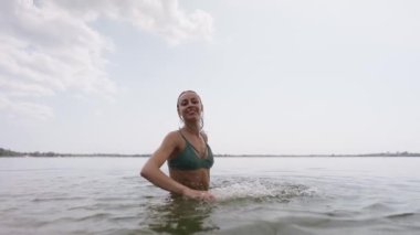 Yeşil mayo giymiş, göl suyunda eğlenen ve elleriyle su sıçratan güzel, neşeli, genç seksi kız. Plajda tropik arka planda bikinili güzel bir kadın vücudu.