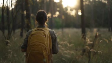 Kamera, güzel ormanda yürüyen ve güzel doğayı keşfeden genç bir kadını takip ediyor. Sarı sırt çantalı ve tişörtlü. Kamerada güneş parlıyor, mercek parlıyor..