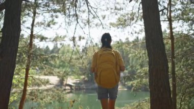 Kadın turist, güneşli bir sonbahar gününde sonbahar ormanında yolda yürüyor. Sarı sırt çantalı kadın yürüyüşçü güneşli bir sabahta dağ gölünün etrafındaki ormanda yürüyüş yapıyor. Açık hava macerası..