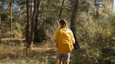 Kadın turist, güneşli bir sonbahar gününde sonbahar ormanında yolda yürüyor. Sarı sırt çantalı kadın yürüyüşçü güneşli bir sabahta dağ gölünün etrafındaki ormanda yürüyüş yapıyor. Açık hava macerası..