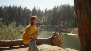 Kadın turist, güneşli bir sonbahar gününde sonbahar ormanında yolda yürüyor. Sarı sırt çantalı kadın yürüyüşçü güneşli bir sabahta dağ gölünün etrafındaki ormanda yürüyüş yapıyor. Açık hava macerası..