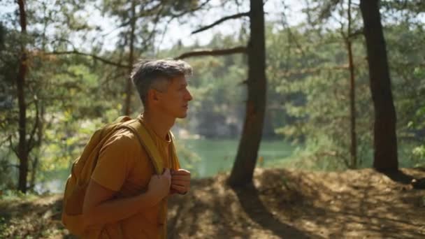 秋天阳光明媚的日子 人类游客在秋天的森林里走着小径 男子徒步旅行者 背着黄色背包 阳光明媚的早晨在山湖周围的森林里徒步旅行 冒险户外生活 — 图库视频影像