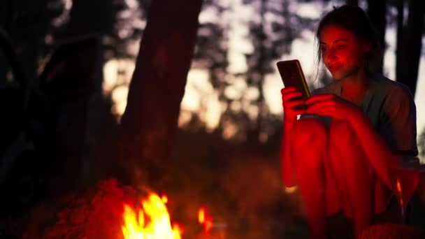 Hipster Girl Using Smartphone Sitting Next Bonfire Forest Camping Night — Stock Video