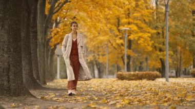 Güneşli bir günde, sonbaharda parkta yürüyen ve gülümseyen çekici esmer bir kadının portresi. Sonbaharda açık havada mutlu ve güzel bir kadının yüzü. Yavaş çekim 4k görüntü