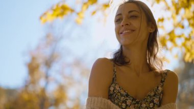 Güneşli bir günde, sonbaharda parkta yürüyen ve gülümseyen çekici esmer bir kadının portresi. Sonbaharda açık havada mutlu ve güzel bir kadının yüzü. Yavaş çekim 4k görüntü