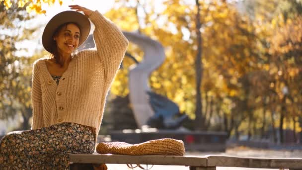 秋天公园的枝头上坐着一位衣着华丽 头戴礼帽的漂亮女子的画像 阳光明媚 面带微笑 秋天的户外 一个快乐美丽的女人的脸 慢镜头4K — 图库视频影像