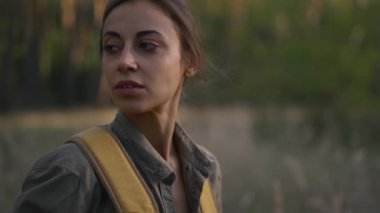 Ormanda sarı sırt çantalı bir turist portresi, etrafa bakıyor, ilham verici, sonbahar havası, sakin bir manzara. Dişi sırt çantalı dışarıda yürüyor.