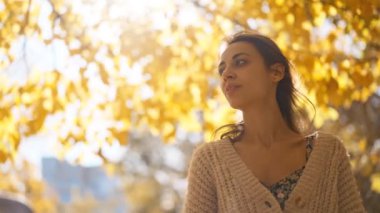 Güzel beyaz bir kızın yakın plan portresi. Bayan gündüzleri güneş ışınlarıyla ayakta duruyor. Doğada yürümekten ve poz vermekten zevk alan bir model, kameraya bakıyor. Sonbahar parkında boş zaman. Görünüm.