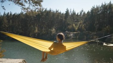 Rahatlamış, bikinili mutlu kadın ormandaki dağ gölü kıyısında hamakta sallanıyor. Seyahat, yaz tatili, açık havada seyahat, boş zaman..