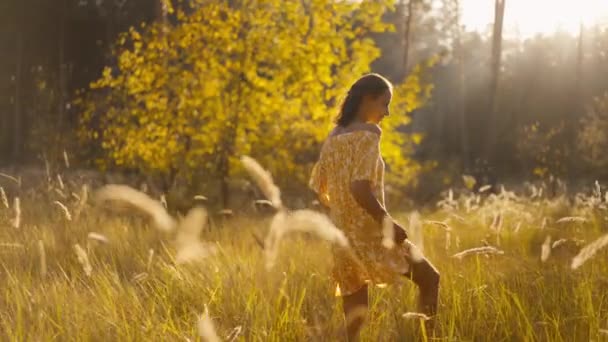 在金黄的秋日落日里 穿着黄色长裙的美丽而悠闲的女人 敞开的双肩漫步在松林里 可爱的女孩在户外散步 享受大自然 — 图库视频影像