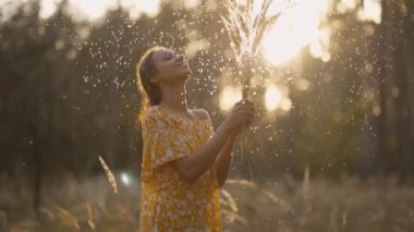 Sarı elbiseli genç bir kadın ormanda günbatımının tadını çıkarıyor. Kuru kabarık çiçekler, dikenler ve karahindibalarla oynuyor. Yaz çimlerinde tüy üfleyen sinematik manzaralı kız. Alerjiden arındırılmış konsept