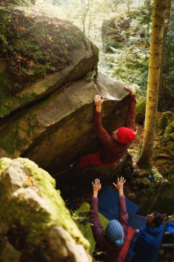 Kırmızı kayalıklardaki kaya tırmanışçısı sakin ormandaki kayalara tırmanıyor. Aktif yaşam tarzı, güç, kararlılık ve açık hava macerası kavramı