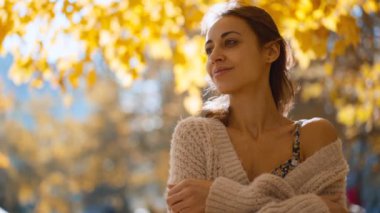 Güneşli bir günde, sonbaharda parkta yürüyen ve gülümseyen çekici esmer bir kadının portresi. Sonbaharda açık havada mutlu ve güzel bir kadının yüzü. Yavaş çekim 4k görüntü