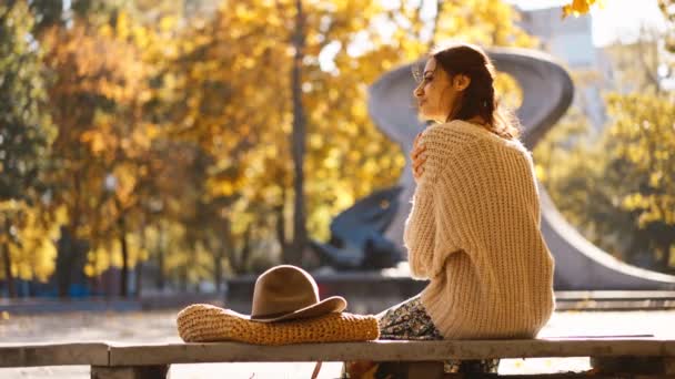 穿着衣服 毛衣和帽子的美丽微笑的女人的秋天画像 黄色叶背的女孩看着摄像机 — 图库视频影像