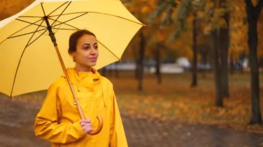 Sarı şemsiyeli kız. Ağır çekim yağmur parkı. Şemsiyenin altında yağmur damlasından saklanan genç kadın. Çamurlu yürü. Sağanak yağmur. Kötü bulutlu hava. Kadınlar ıslak caddede yürürler.
