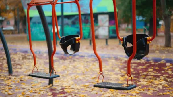 子供のためのアトラクションを持つ市立公園の雨の秋の日 濡れた黄色いメープルは地面に葉 空っぽのベンチと遊び場でスイングします 落ちる 悲しい気分 — ストック動画