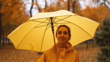 Sarı şemsiyeli kız. Ağır çekim yağmur parkı. Şemsiyenin altında yağmur damlasından saklanan genç kadın. Çamurlu yürü. Sağanak yağmur. Kötü bulutlu hava. Kadınlar ıslak caddede yürürler.