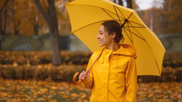 黄色い傘を持っている少女 スローモーションレインシティパーク 人種差別から傘の下に隠れている若い女性の側面 スラッシュを歩く 雨が降る 悪天候だった 女性は濡れた通りに沿って歩きます — ストック動画