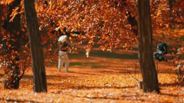 Yavaş çekim soyut sonbahar sahnesi. ön planda kırmızı ve turuncu yapraklar rüzgarla hareket eden dallarda. Bulanık arka planda yürüyen kadın hakkında