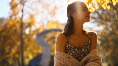 Güneşli bir günde, sonbaharda parkta yürüyen ve gülümseyen çekici esmer bir kadının portresi. Sonbaharda açık havada mutlu ve güzel bir kadının yüzü. Yavaş çekim 4k görüntü