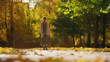 Uzun örülü süveter ya da hırka giyen bir kadın altın yapraklı doğal akçaağaç parkında yürüyor. Doğadaki kadın sıcak sonbahar gününde. Aktif yaşam tarzı. Açık havada bir kadın. Kız sonbahar parkında yürüyor.