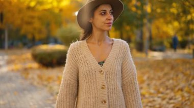 Uzun örgü süveter giyen neşeli, güler yüzlü kadın ya da altın yapraklı akçaağaç parkında yürüyen hırka. Doğadaki kadın sıcak sonbahar gününde. Aktif yaşam tarzı. Açık havada bir kadın. Kız sonbahar parkında yürüyor.
