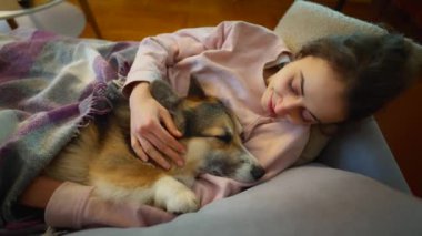 Sevecen kadın köpek sahibi kanepeye uzanmış, şirin, komik Galli Corgi köpeğiyle rahat bir odada. Evcil hayvanı olan bir kız, battaniyeli. Uykulu köpeği okşayan şefkatli bir kadın. Dört bacaklı bir arkadaşla yaşıyor..